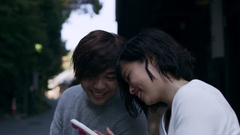 Young couple sitting outside and looking on the girlfriend's phone happily in Kyoto, Japan with soft natural lighting. Close up to wide shot on 4k RED camera on a gimbal.