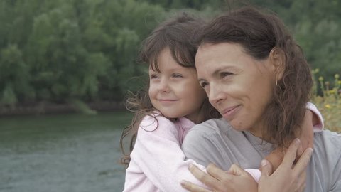 Portrait of a woman with a child. Happy daughter hugs mother. Charming little girl with mom on nature.