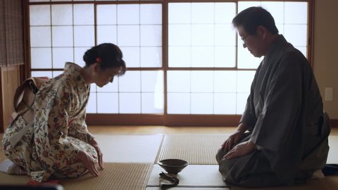 Authentic male tea master serving a bowl of hot matcha tea to a smiling geisha in a traditional Japanese room with soft day lighting. Medium shot on 4k RED camera on a gimbal.