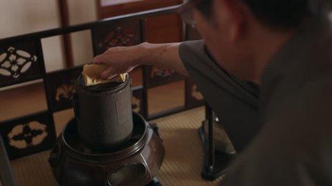 Master tea maker taking the lid off of a pot of steaming water in a traditional Japanese home with soft day lighting. Close up shot on 4k RED camera on gimbal.