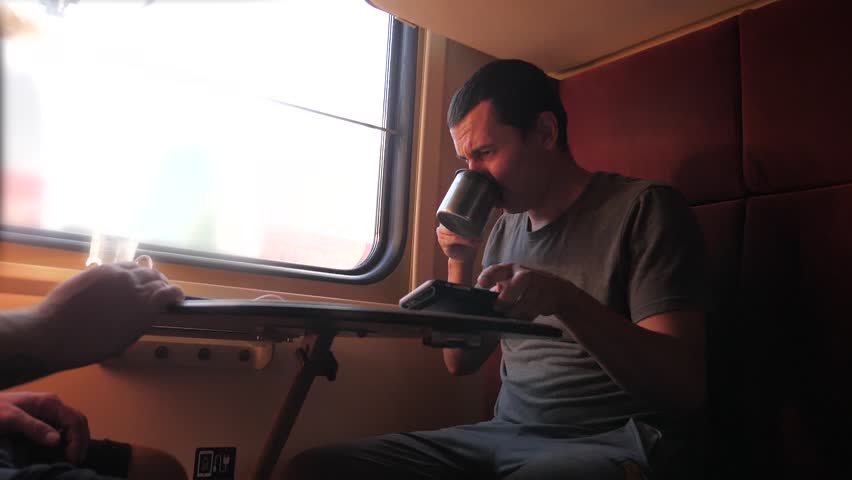 man is sitting on the train carriage holding a smartphone Railway and drinking coffee and tea. slow motion video. man writes messages in the smartphone in the train social media. man with smartphones