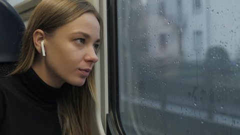 Woman with headphones in a bus train. Portrait of a woman passenger tourist. A woman listens airpods music headphones dreaming rainy day.