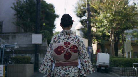 Back view of woman in kimono walking down a quiet residential street in a kimono in Japan, with soft day lighting. Medium shot on 4k RED camera.