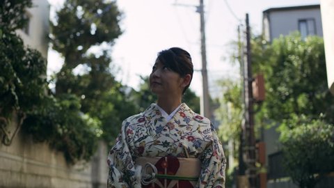 Smiling female wearing traditional floral kimono walking down a quiet residential street in Japan, with soft day lighting. Medium shot on 4k RED camera.