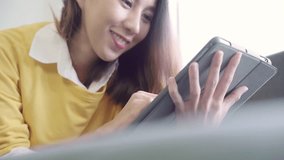 Beautiful Asian woman using tablet watching video while wear sweater lying on sofa in living room at home. Lifestyle woman at home concept.