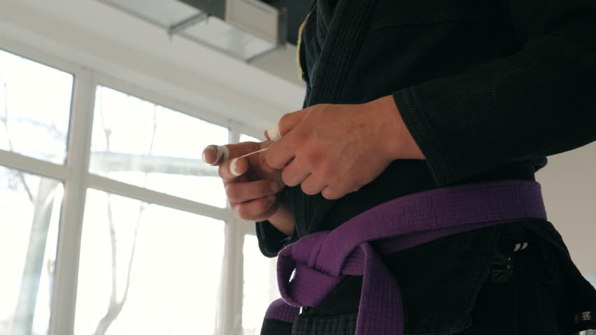 man in kimono standing with her back preparing for mma fight fingers tape hand close up sun flares
