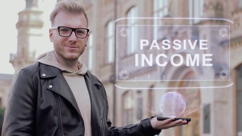 Smart young man with glasses shows a conceptual hologram Passive income. Student in casual clothes with future technology mobile screen on university background