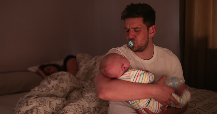 Dad checking on his newborn son, during the night, while his wife is fast asleep behind his on the same bed that he is sitting on to check his newborn. Royalty-Free Stock Footage #1019883121