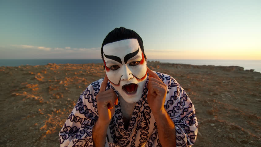 Musician and artist Josh Rawiri in Kabuki makeup in surreal scene at sunset overlooking clifftop.
