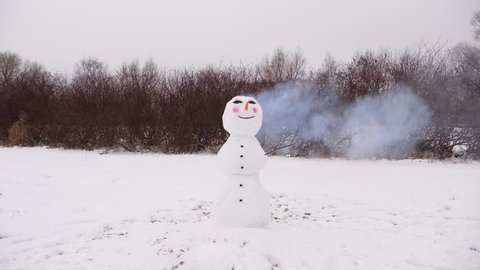 Funny smiling face of snowman, head of snow figure blowing up by cracker detonation. Hard stress and overwork concept, top ball of snow man explode and break apart, parts scatter around