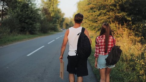 Couple On Vacation Hitchhiking Along Road and Holding Adventure Sign. Summer time. Hitchhiking, tourists, adventures concept