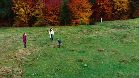 Mom and her children play with the ball in the autumn forest. They fun run and throw each other a ball. The family is happy. Outdoor activities. Slow motion. Shooting from the drone.