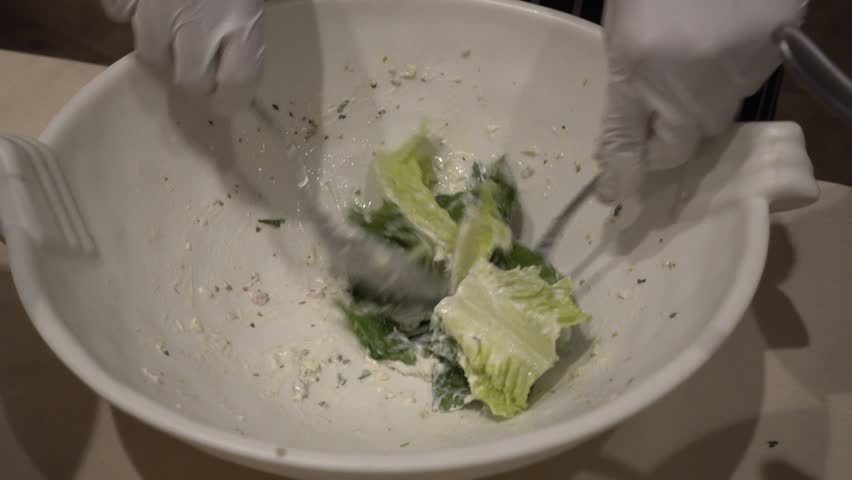 Closeup of young woman mixing green salad in wooden bowl at table with wholesome food while preparing family dinner of night party. cooking food concept.