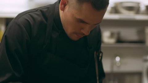 Professional chef placing lettuce onto a wooden plate with tomatoes and cheese for serving in industrial kitchen with soft lighting. Close up shot on 4k RED camera.