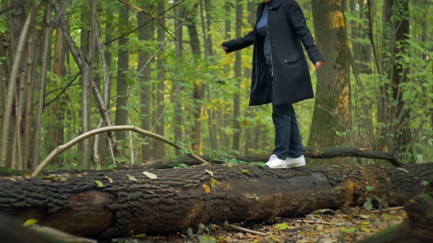 girl in a blue turtleneck and red hair in white sneakers, goes along the log of a fallen tree