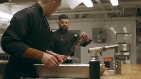 Group of professional chefs prepping food in industrial kitchen with soft interior lighting. Close up shot on 4k RED camera on a gimbal.