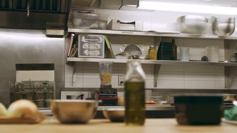 Pan of kitchen tools including bowls and cutting board with vegetables on counter in industrial kitchen with soft lighting. Close up shot on 4k RED camera on a gimbal.