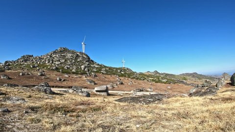 Eco Theme, detailed view at the wind turbines on top of mountain, vegetation and granite stones, blue sky as background