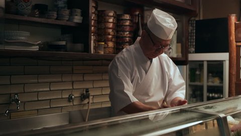 Experienced male sushi chef taking wasabi and rice and making a ball in hands in small traditional sushi bar with soft day lighting. Medium shot on 4k RED camera.