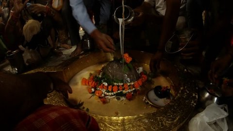 Hands of big crowd of people pour water and milk over swayambhu self-existing lingam and put leaves and flowers in ancient hindu temple Rishikesh