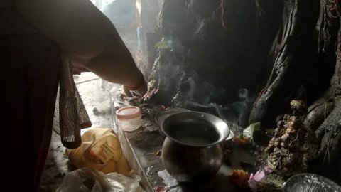 Women's hands worship do puja ritual prayer with lights to old big banyan tree smoke on background legs of people in traditiinal indian clothes ancient hindu temple Rishikesh