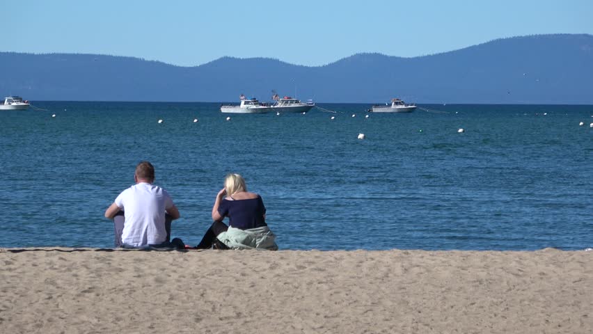 Man and woman sitting on beach at Lake Tahoe watching waves