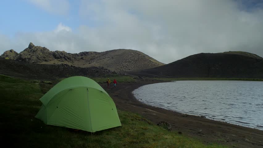 beautiful iceland landscape, two hikers walking together by the lake with a tent pitched in a foreground,