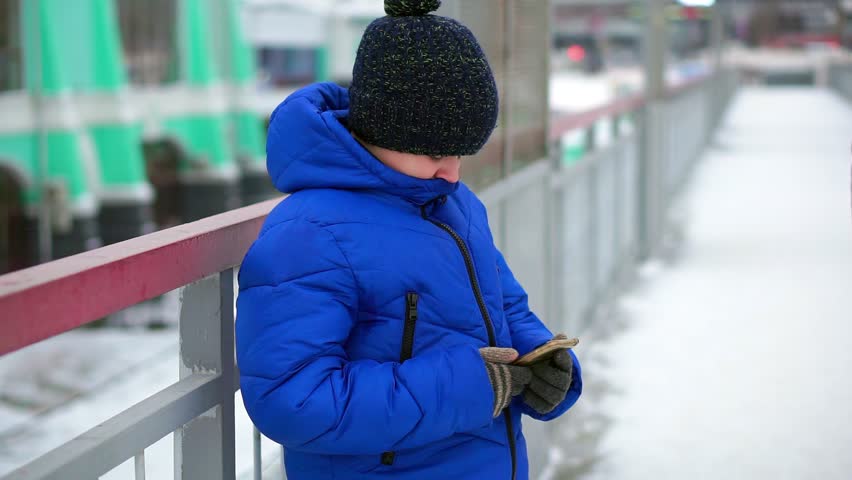 Boy in blue down jacket on the street reads messages smartphone. | Shutterstock HD Video #1019926810