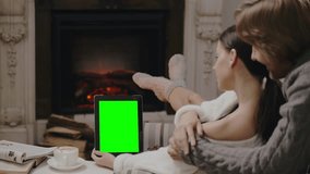 Young couple spending a winter weekend watching the series on tablet computer together indoors. Green screen