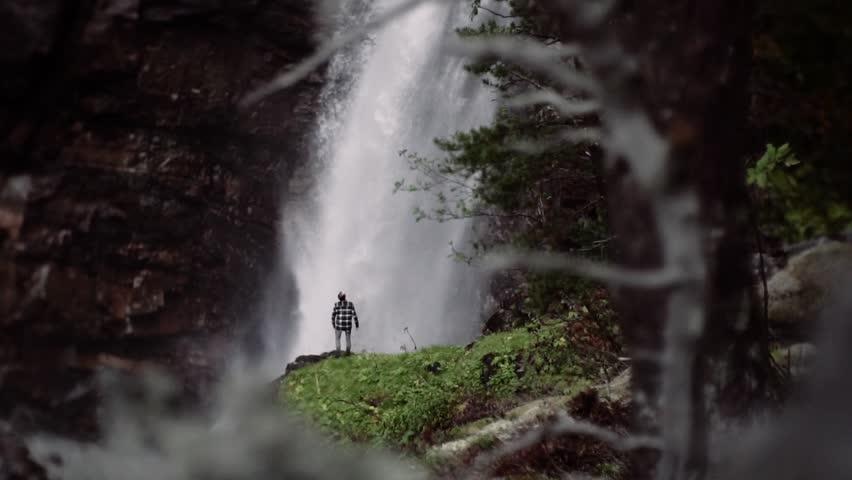 Man standing in front of a huge waterfall, slow motion shot of a beautiful location during day time. Norway, Europe.