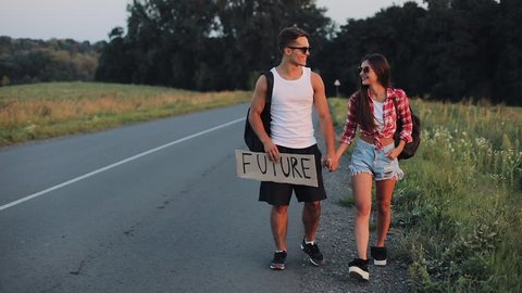 Couple On Vacation Hitchhiking Along Road and Holding Future Sign. Summer time. Hitchhiking, tourists, adventures concept