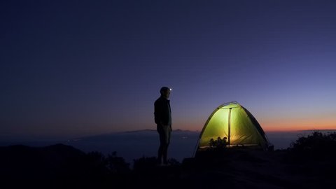 an adult man in an adventure trip to the top of a mountain set up a tourist tent for an overnight stay
