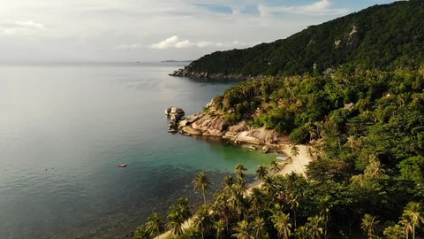 Aerial drone top view of white sand tropical exotic paradise tiny shore in Koh Prangan island, Thailand. Small boats on ocean surface. Cute remote beach with volcanic stones and green coconut palms.