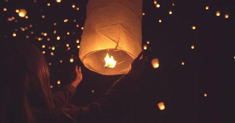 Happy young woman releasing lit paper lantern at night during lantern festival