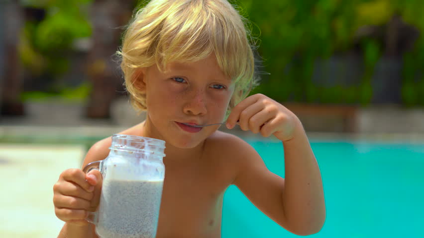Little boy eats a chia pudding sitting on a side of a pool