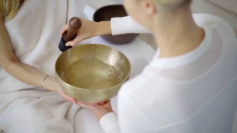 physician woman is touching and rotating stick-resonator around metal bowl in nada therapy