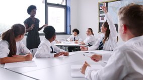Female High School Tutor Asking Pupils Wearing Uniform Sitting At Desks Question To Which They Raise Their Hands - Powered by Shutterstock - Get 15% off with code: PIKWIZARD15