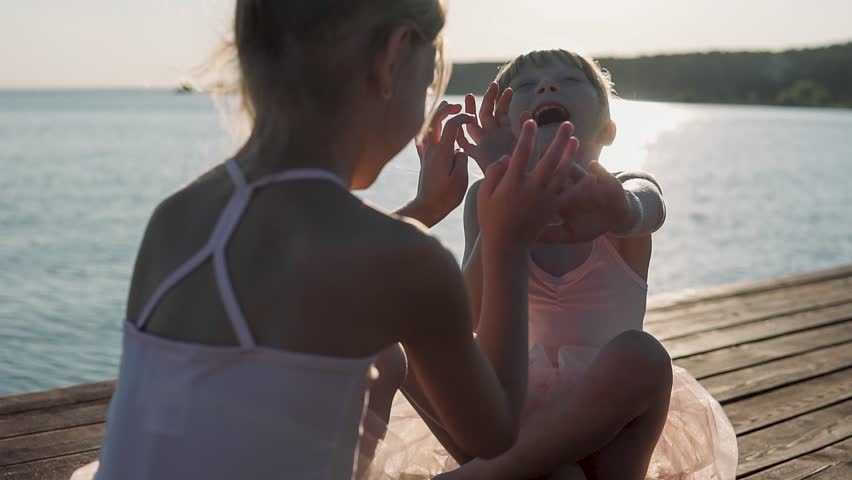Happy girls in beautiful dresses are playing on the sea pier. In the background sea sunset. Wooden pier