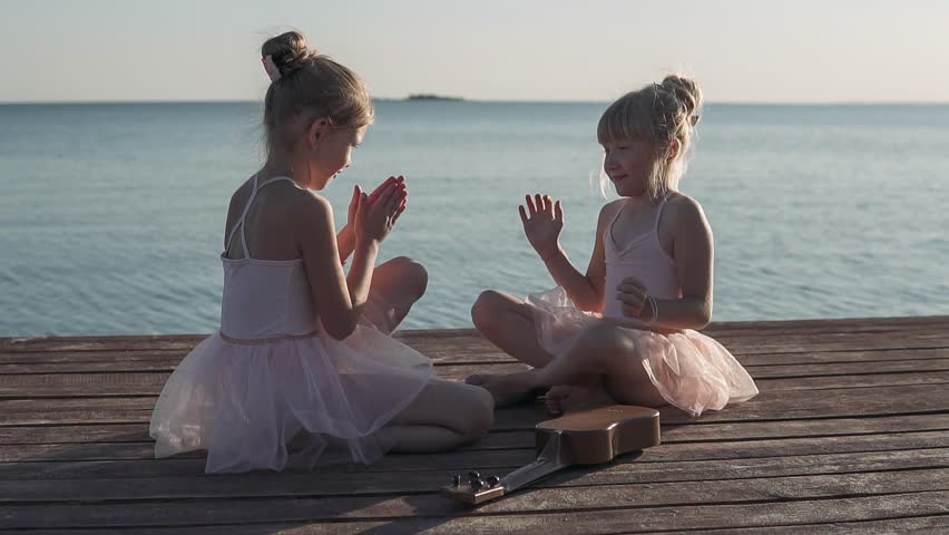 Happy girls in beautiful dresses are playing on the sea pier. In the background sea sunset. Wooden pier