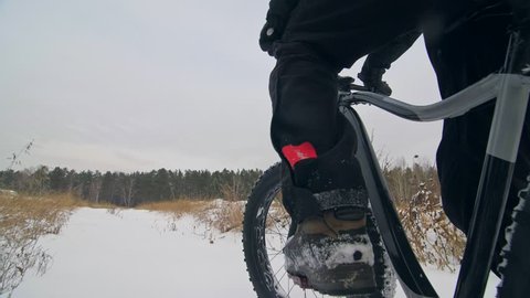 Professional extreme sportsman biker sit a fat bike in outdoors. Cyclist recline in the winter snow forest. Man walk with mountain bicycle with big tire in helmet and glasses. Slow motion in 180fps.