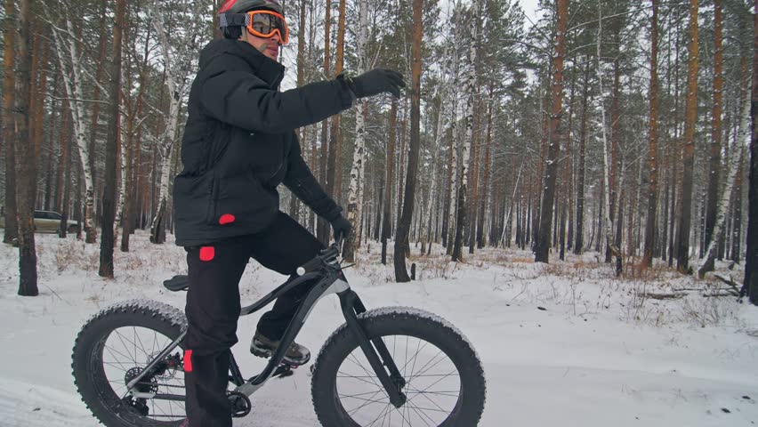 Professional extreme sportsman biker sit a fat bike in outdoors. Cyclist recline in the winter snow forest. Man walk with mountain bicycle with big tire in helmet and glasses. Slow motion in 180fps.