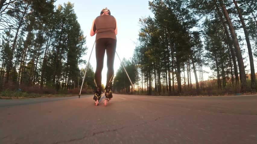 Training an athlete on the roller skaters. Biathlon ride on the roller skis with ski poles, in the helmet. Autumn workout. Roller sport. Adult man riding on skates. Shooting action cam. Slow motion.