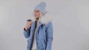 Portrait of a young girl in a warm winter jacket with a cup of coffee, a woman is drinking from a glass, isolated white background, video in slow motion