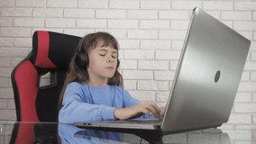 A child at the laptop with headphones. The little girl at the computer listens to music.