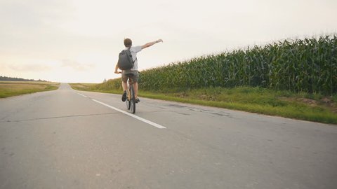 Shows the Yes sign. Young man Cyclist on road bike in sunset at cornfield. Slow motion