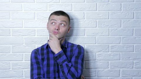 Young adult business man standing over white brick wall serious face thinking about question