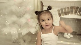 little girl with two tails dancing funny on the background of fireplace and Christmas tree