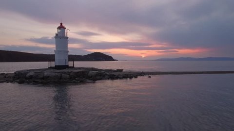 Beautiful Tokarevsky lighthouse on sand bar. Romantic purple sunset clouds Seagulls fly by Calm Ocean Sea. Russia Vladivostok Asia. Navigation happiness peace of mind. Aerial Drone flying forward