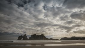 Spectacular cloudscape above beautiful Wharariki Beach in New Zealand with natural archway in coastal rocks. Timelapse video.