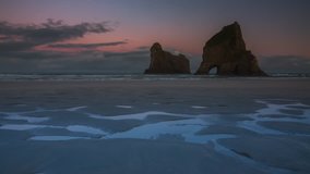 Timelapse video of early morning and sunrise on a beautiful and remote Wharariki Beach in New Zealand with spectacular natural archway in coastal rocks.